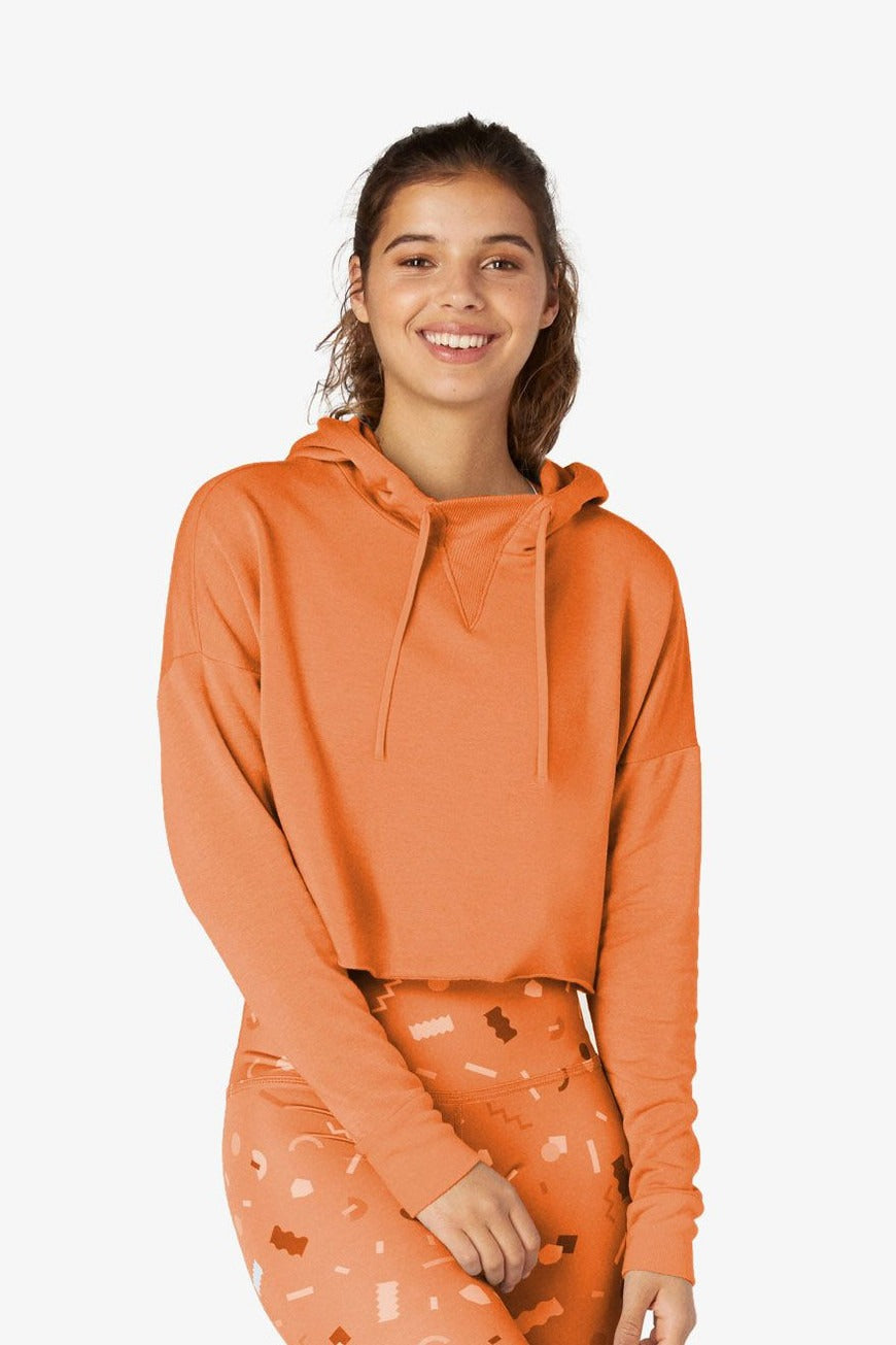 Woman wearing an orange hoodie and patterned leggings on a white background