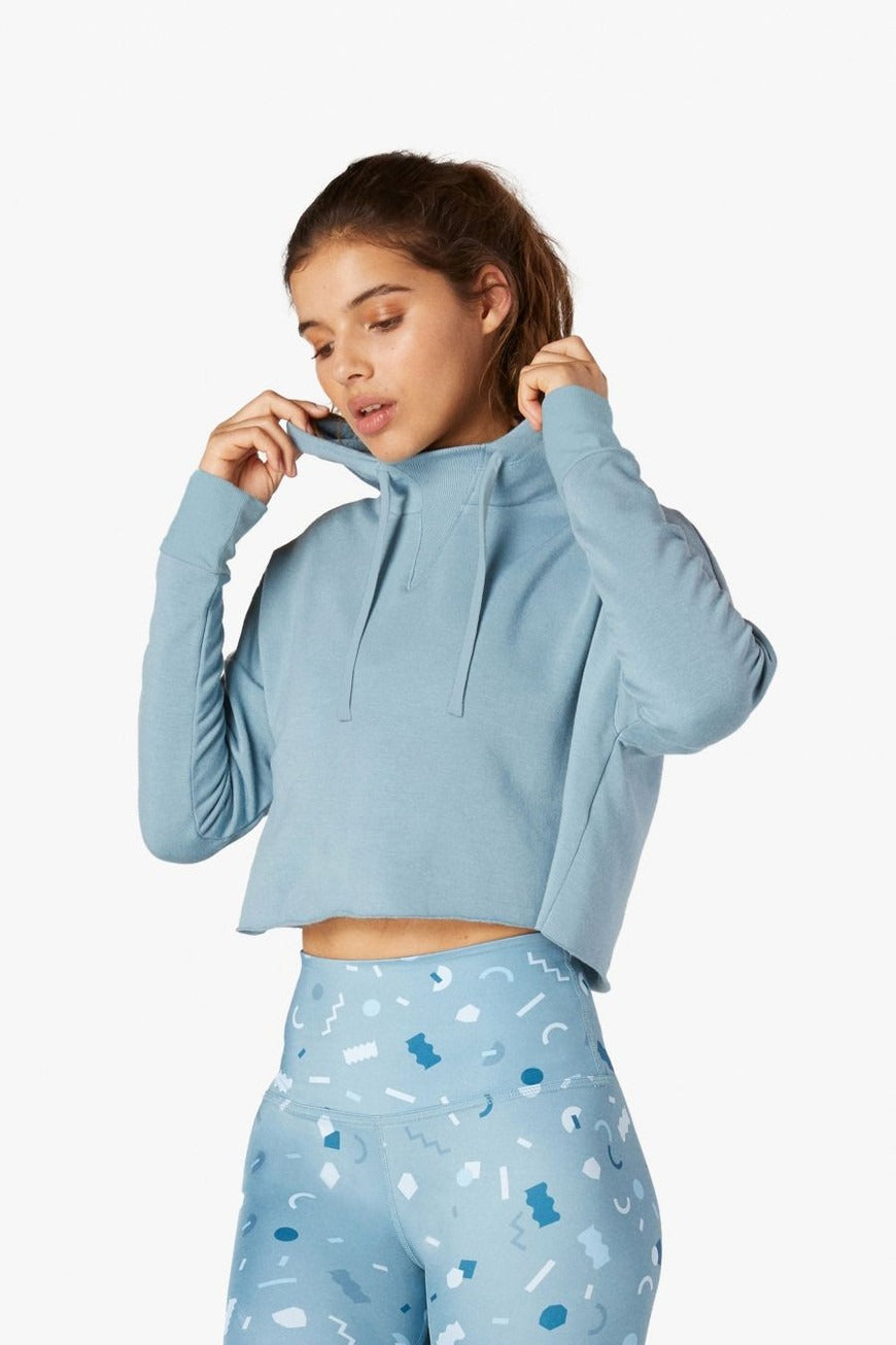 Woman wearing a light blue hoodie and patterned pants on a white background