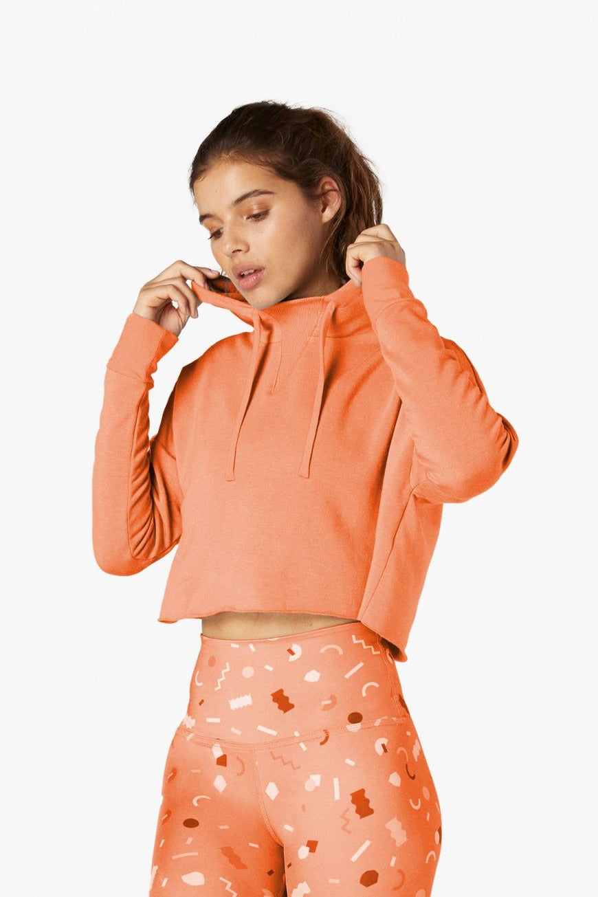 Woman wearing an orange hoodie and patterned leggings on a white background