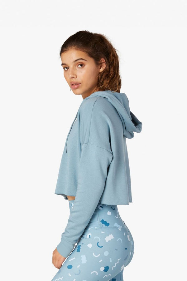 Woman wearing a light blue hoodie and patterned pants on a white background