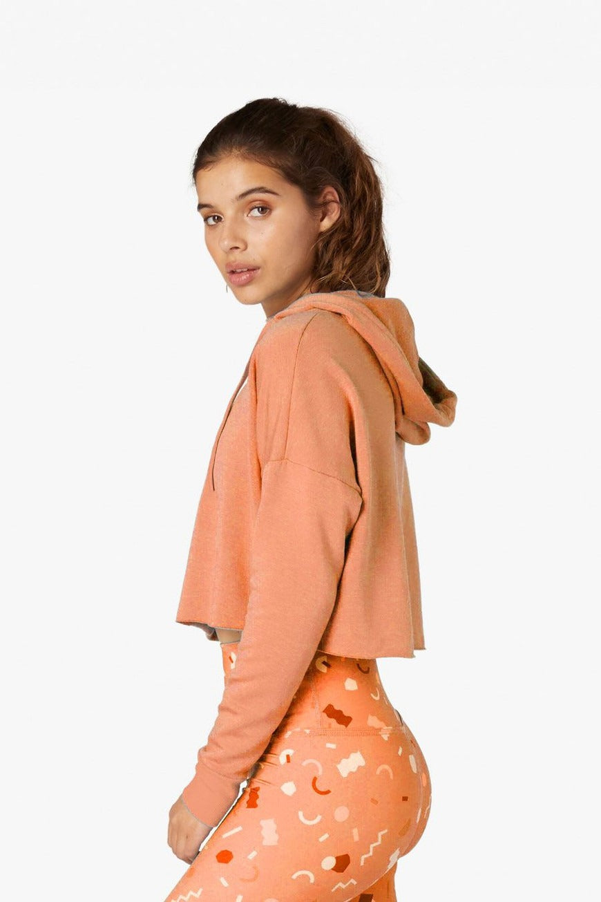 Woman wearing an orange hoodie and patterned leggings on a white background